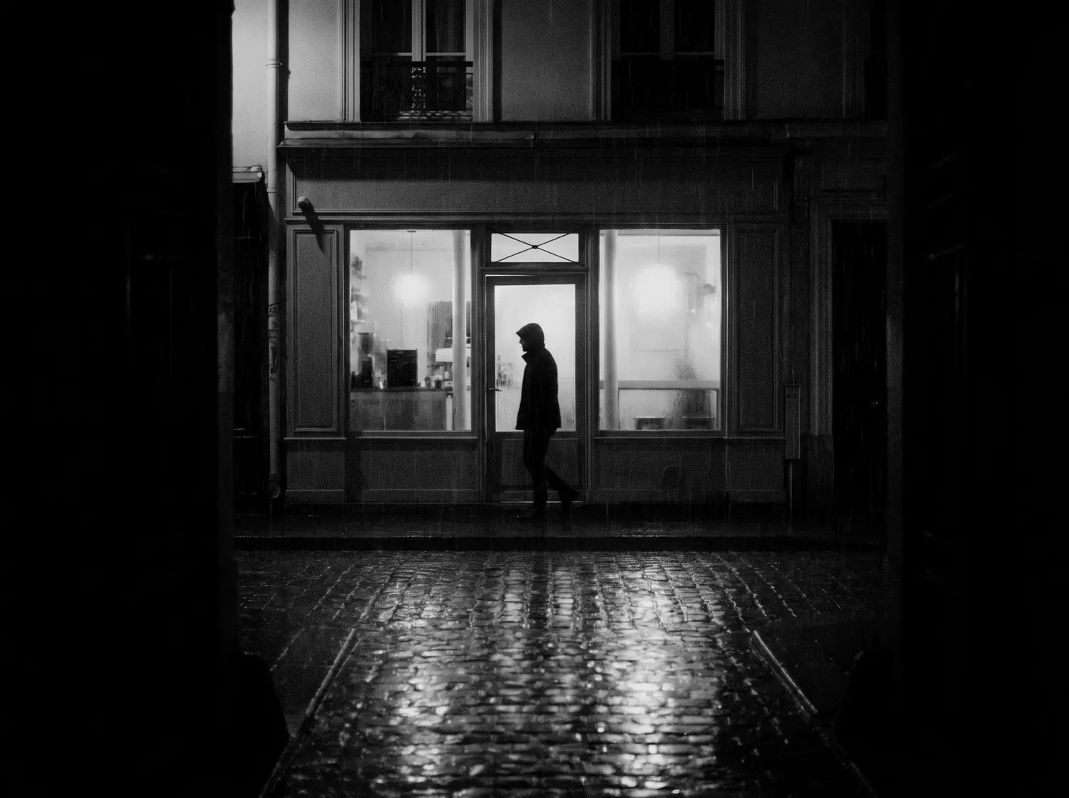 A neighbourhood cafe glowing on a rainy street at night