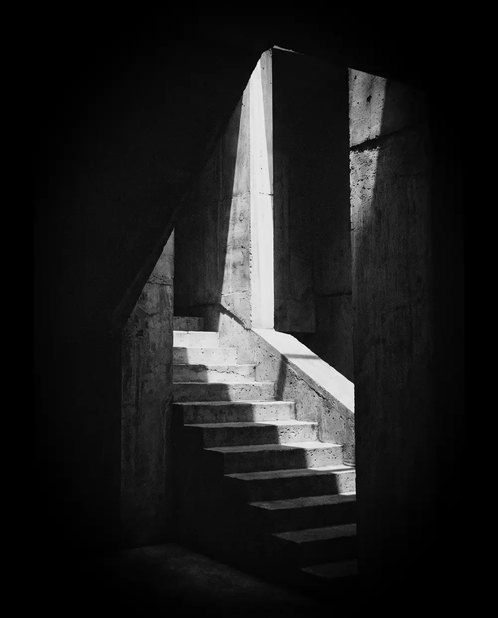 A concrete staircase rising into a shaft of daylight