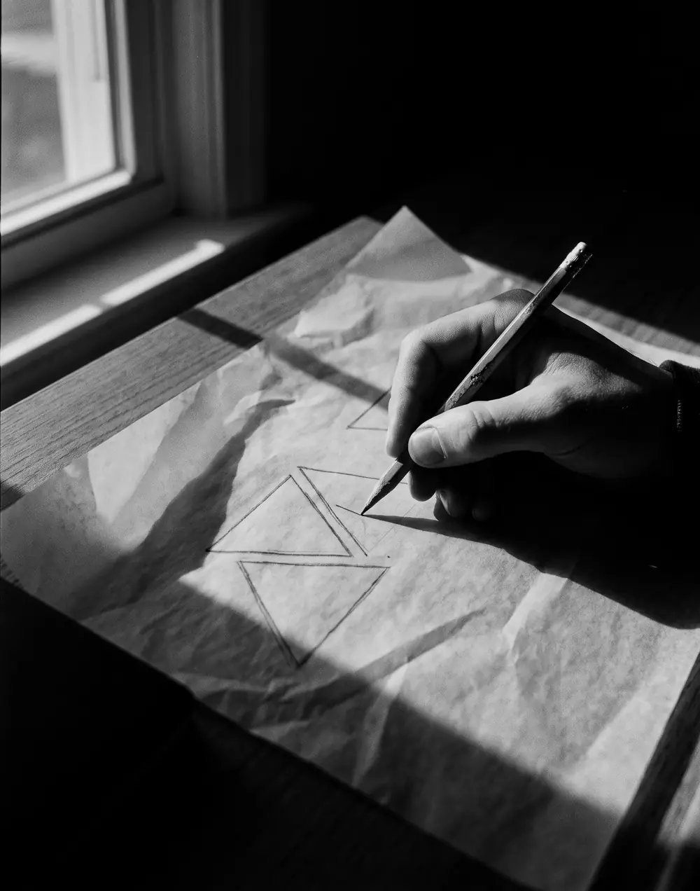 A hand sketching triangles on tracing paper in window light